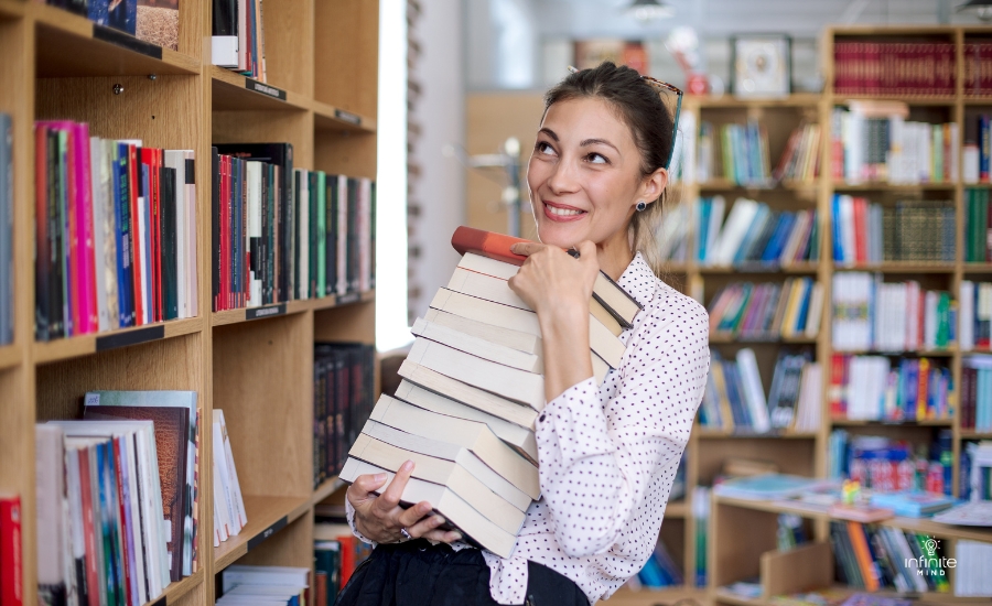 happy-young-woman-with-a-stack-of-books-in-library