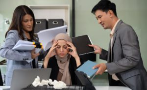 Woman looking stressed in a desk, one man on her right and one woman on her left