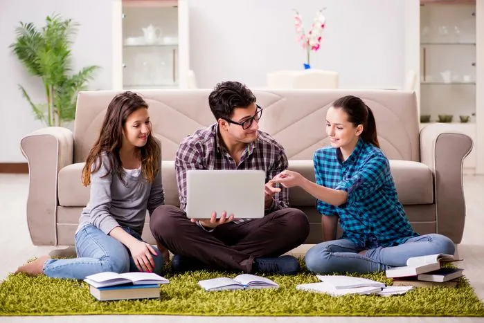 A view of three people studying together with a laptop and books in a cozy living room, enhancing focus and learning.