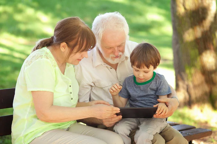 An image of an older couple and a young child sitting on a park bench looking at a tablet outdoors learning about cognitive enhancement.