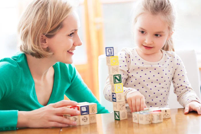 a view of a woman and a young girl building a tower with wooden alphabet blocks improving visual spatial intelligence